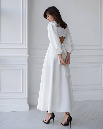 Woman wearing a white dress with cut-out back in a minimalistic room.