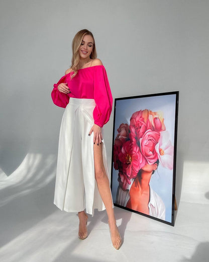 Woman in pink top and white skirt standing next to a framed artwork of a woman with flowers on her head.