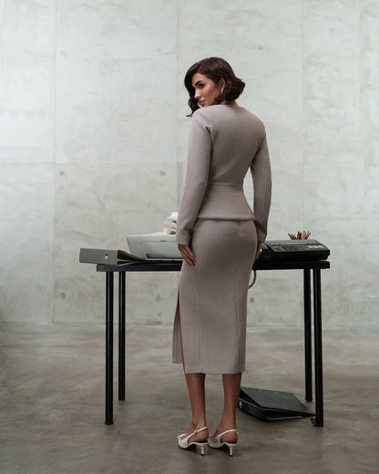 Woman in a gray suit standing in front of a minimalist desk with a concrete wall background