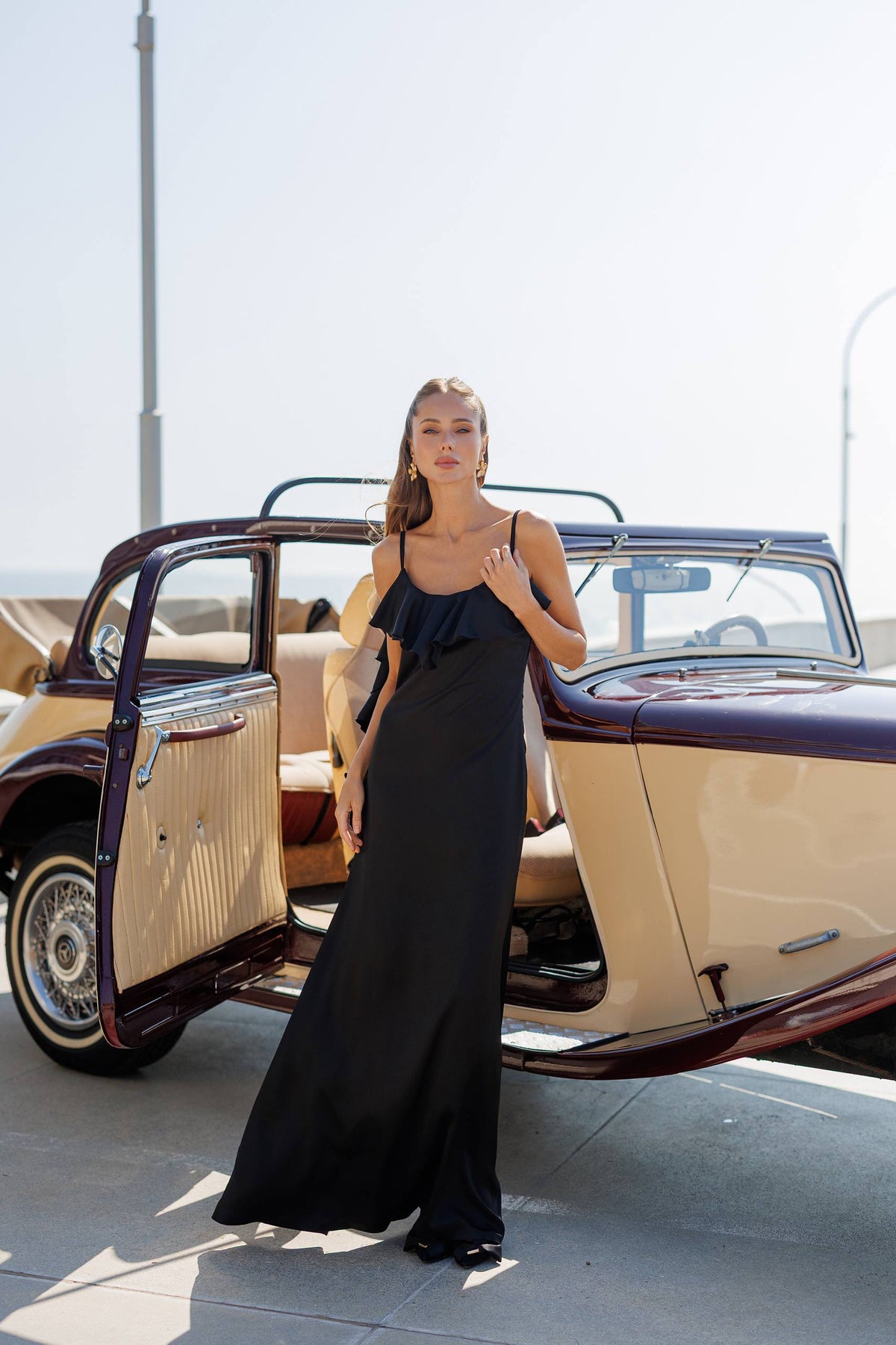 Woman in a black dress standing next to an old-fashioned car