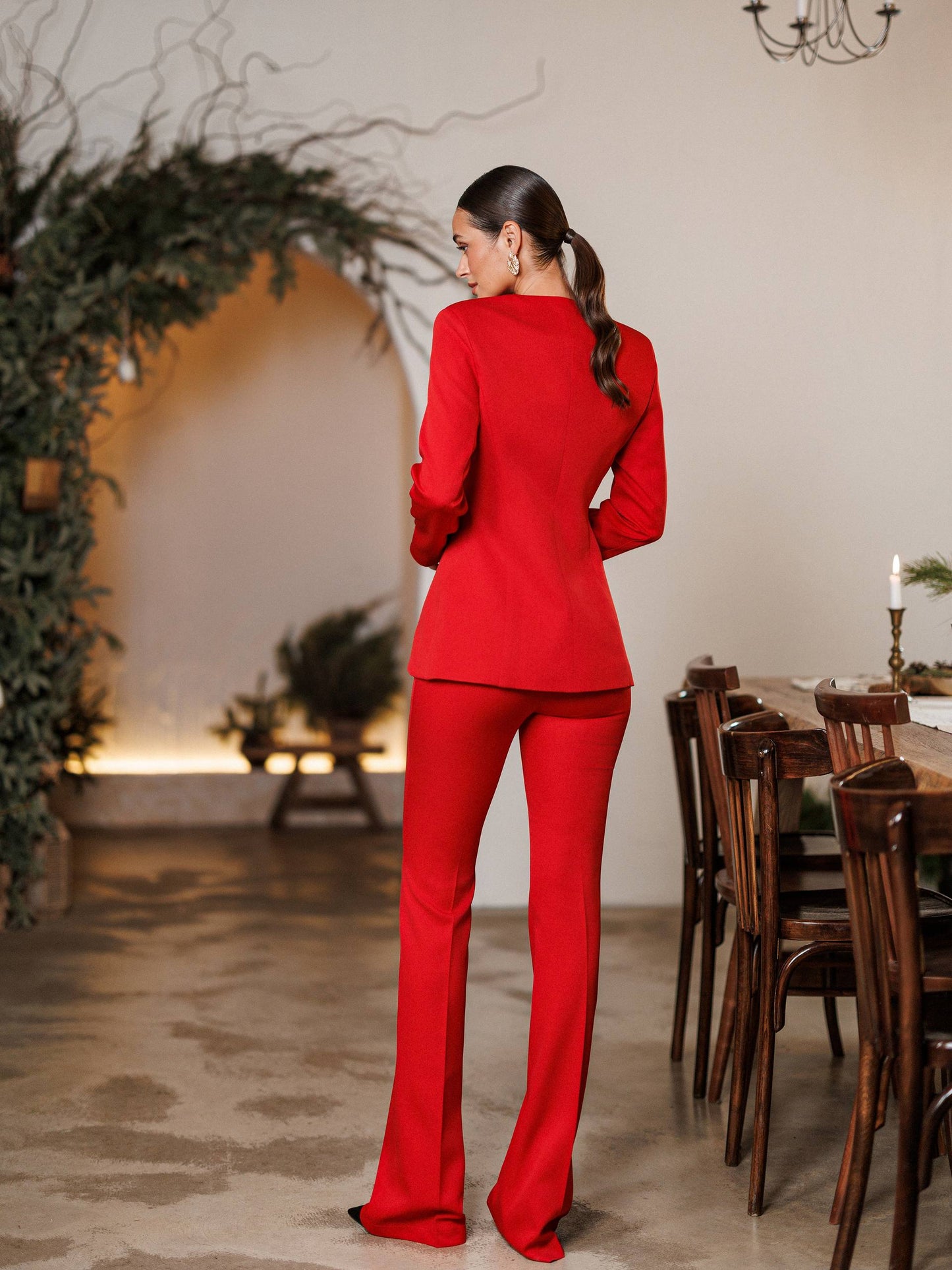 Woman in a red outfit standing in a room with a dining table and decorative plants.
