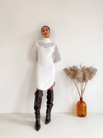Person wearing a white dress with sheer sleeves and black knee-high boots, standing against a plain background.