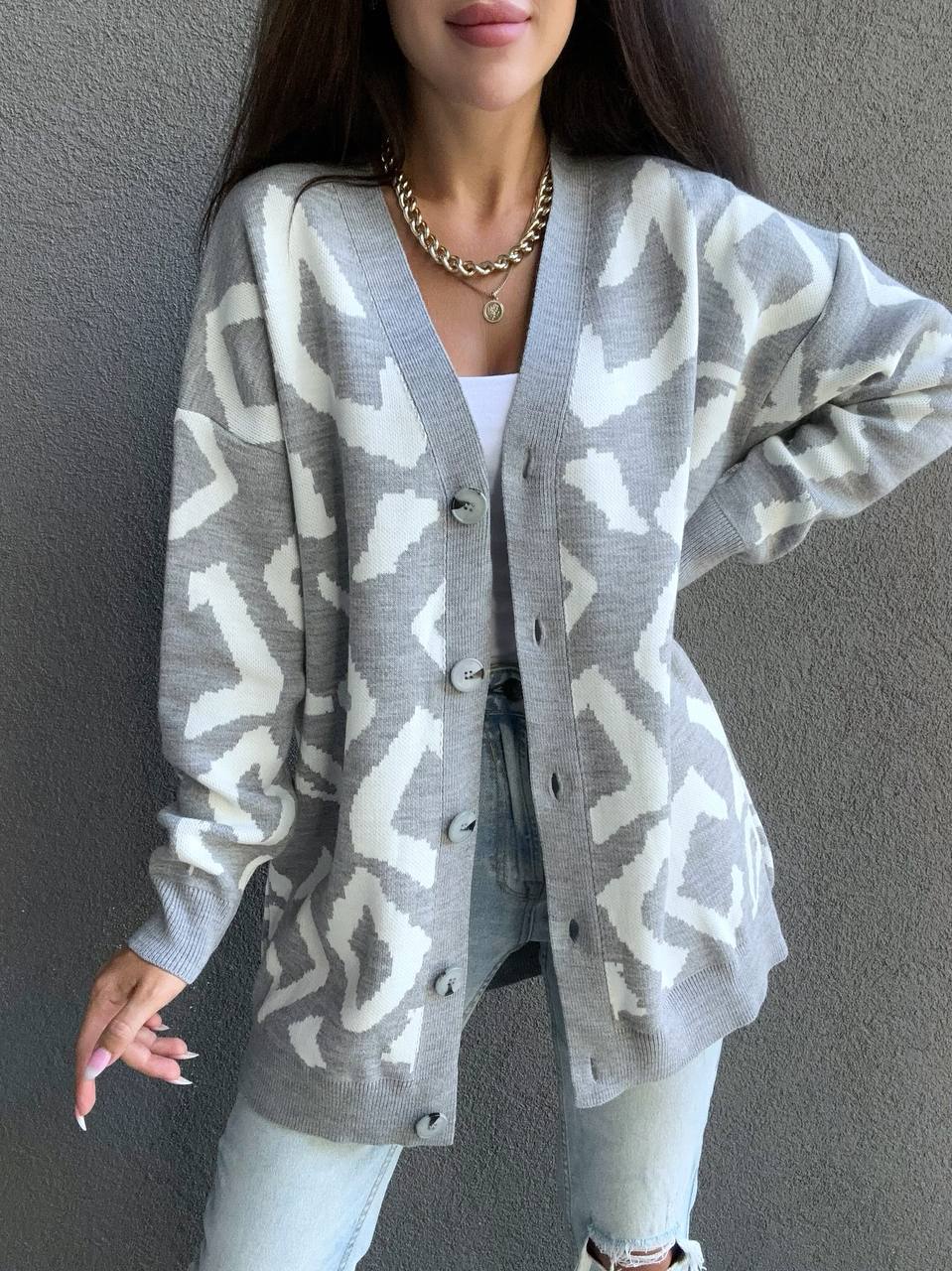 Person wearing a gray patterned cardigan against a plain background