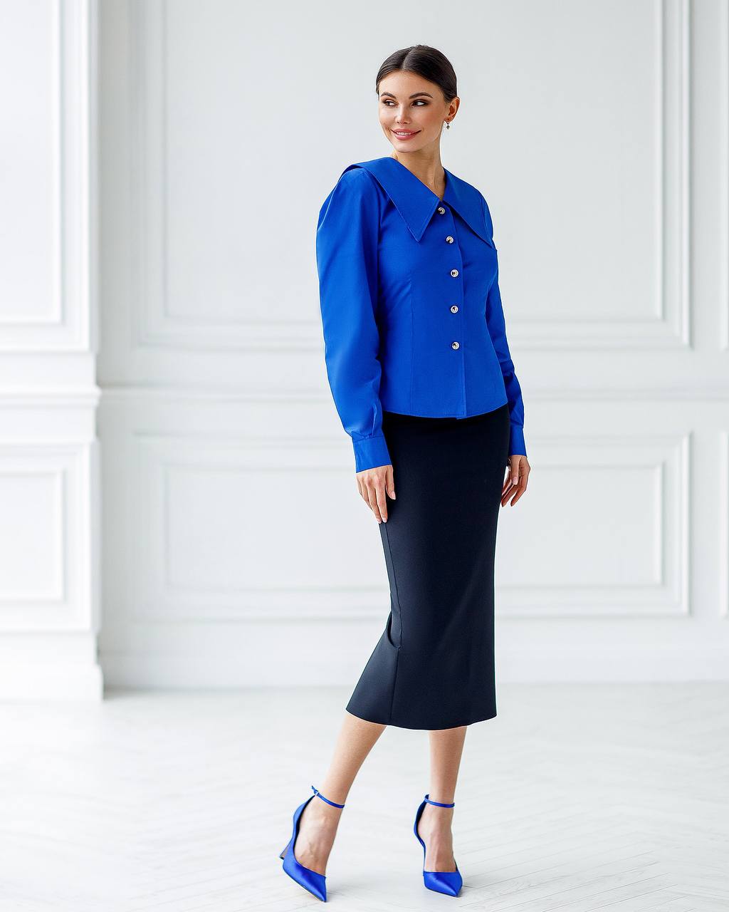 Woman wearing a blue blouse and black skirt against a white wall