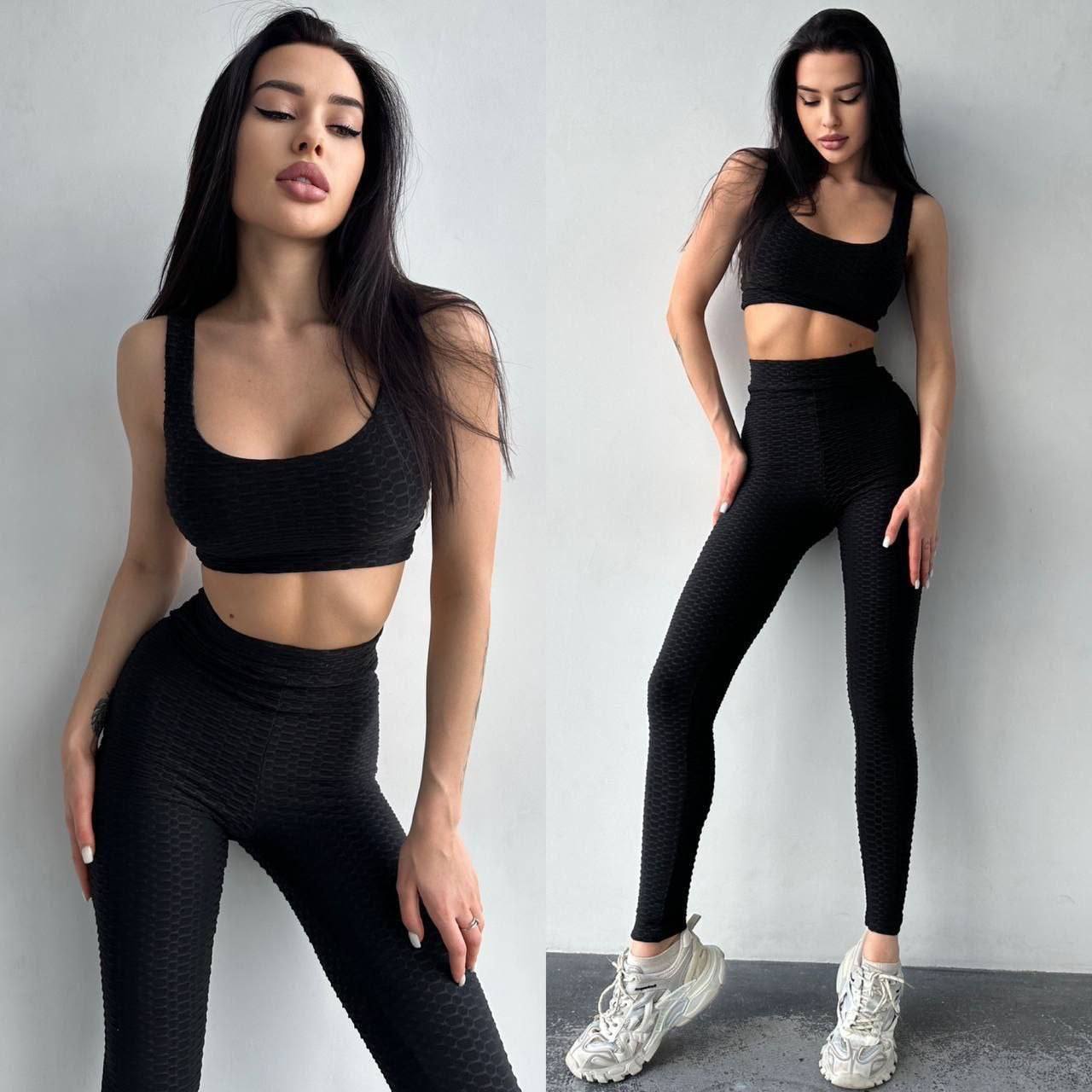 Woman wearing a black athletic outfit with white sneakers against a gray background