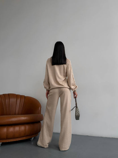 Person wearing a beige outfit standing in a room with a brown leather chair.