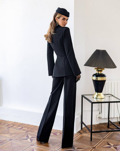 Woman in a black suit standing in a room with a lamp on a table.