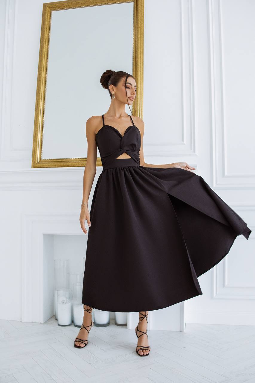 Woman wearing a black dress standing in a room with white walls and a gold-framed mirror.