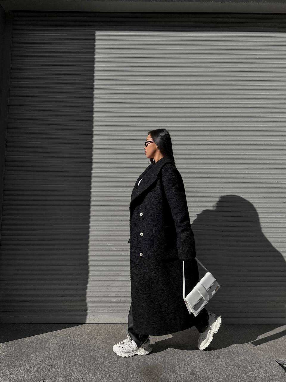 Person wearing a black coat walking in front of a gray shutter.