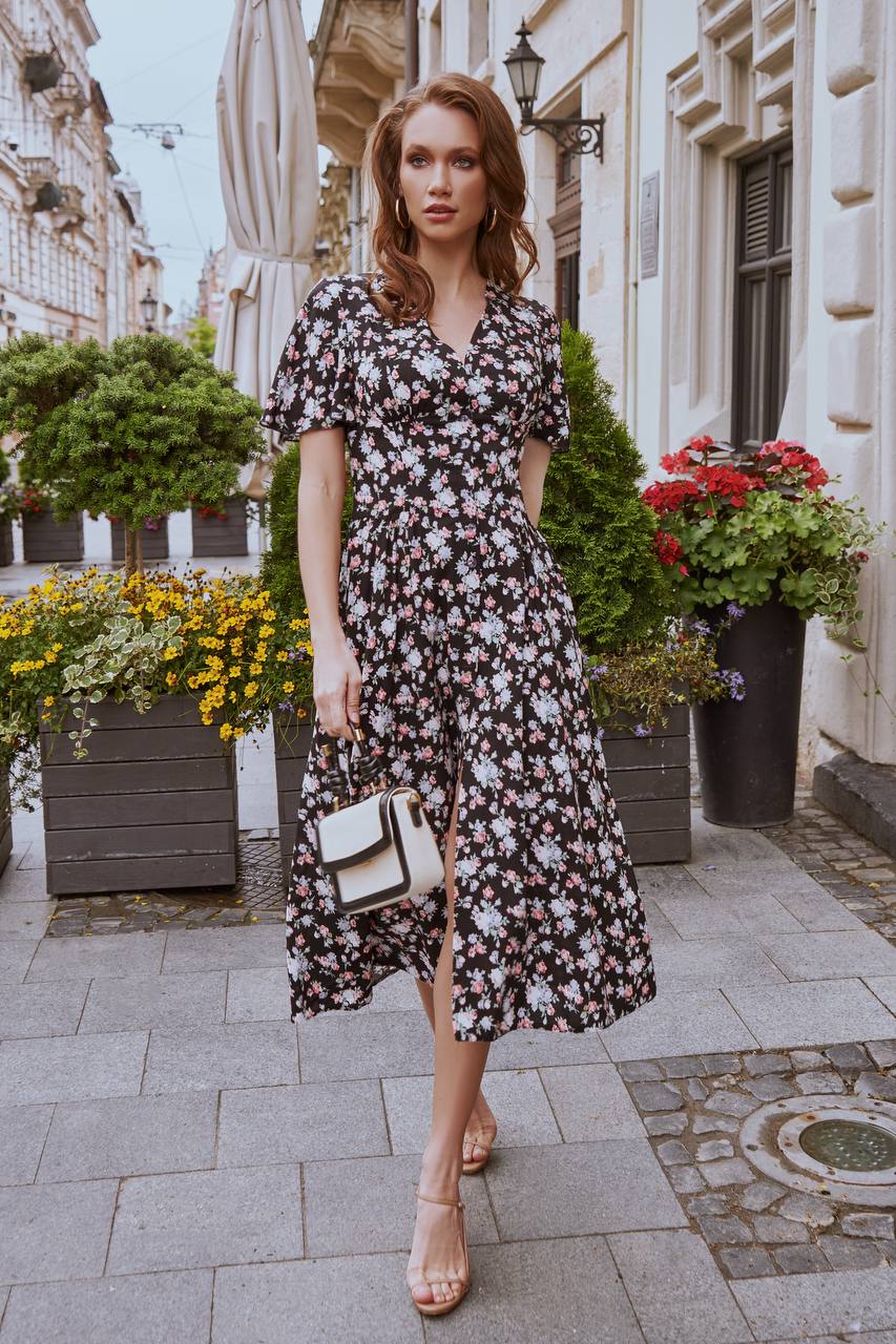 Woman in a floral dress standing on a city street with flowers and plants around.