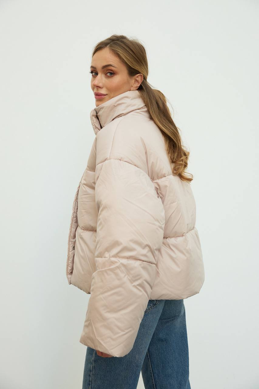 Woman wearing a beige puffer jacket against a white background