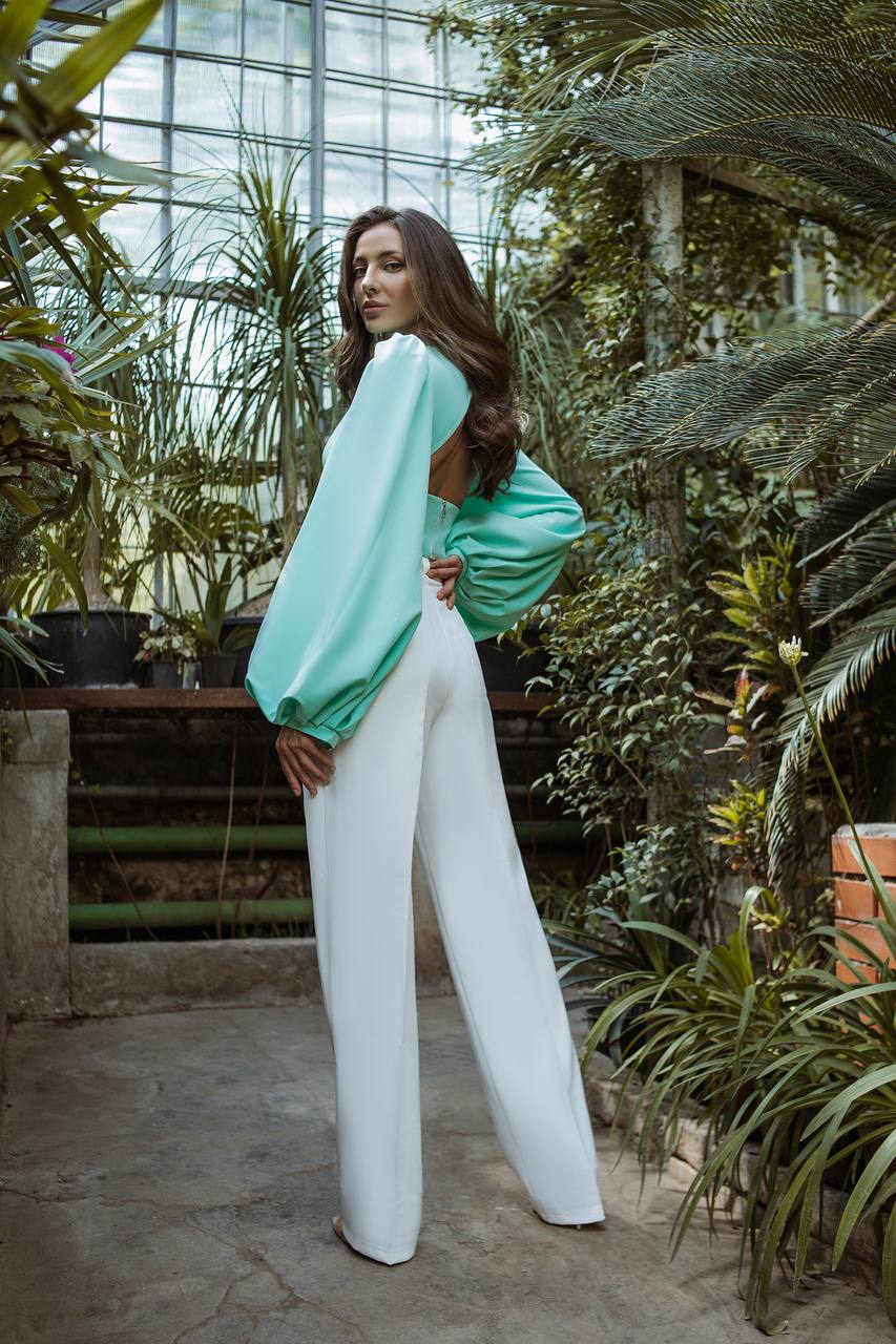 Woman in a green top and white pants standing in a greenhouse.