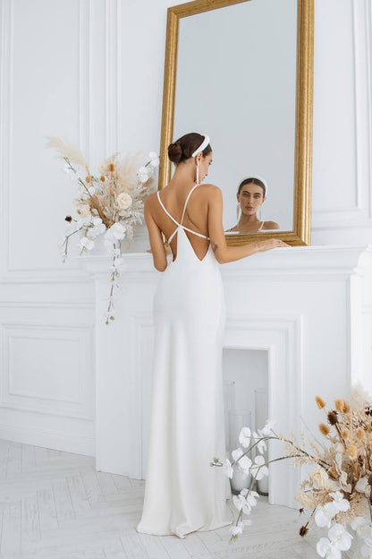Woman in a white dress standing in front of a mirror in a room with decorative flowers.