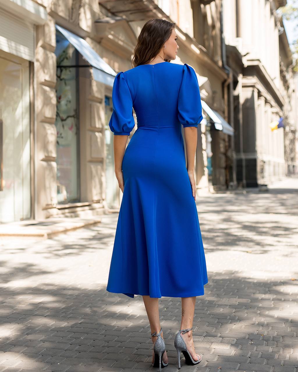 Woman in a blue dress walking down a sunlit street.