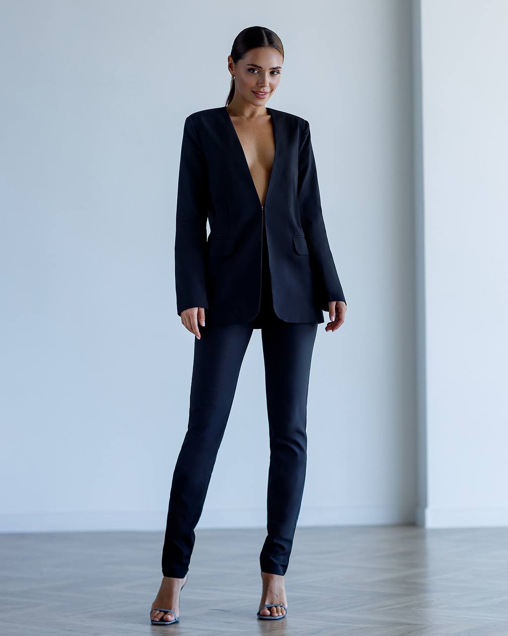 Woman wearing a black suit with a plunging neckline against a plain background
