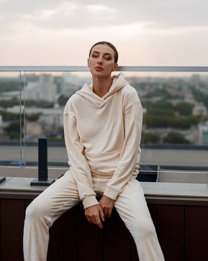 Person wearing a cream-colored hoodie and pants sitting on a ledge with a cityscape in the background