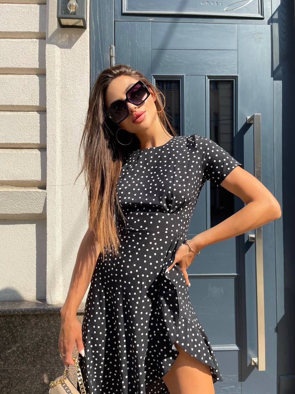 Woman in a black polka dot dress standing in front of a blue door.