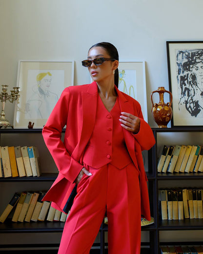 Person wearing a red suit standing in front of a bookshelf with decorative items.
