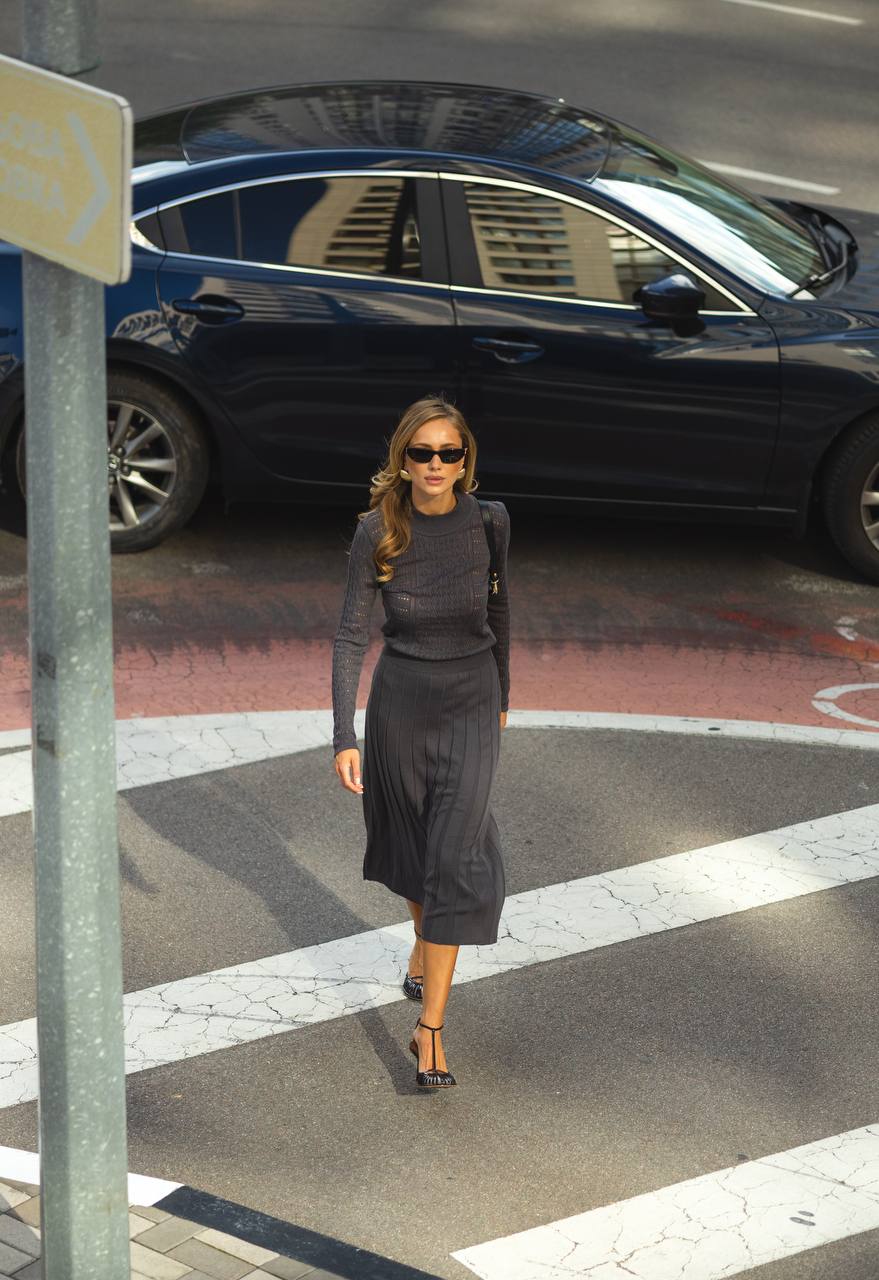 Woman in a gray outfit crossing a street with a black car in the background