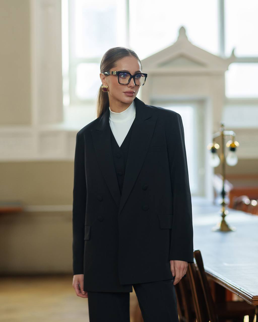 Woman wearing a black suit and glasses in an indoor setting