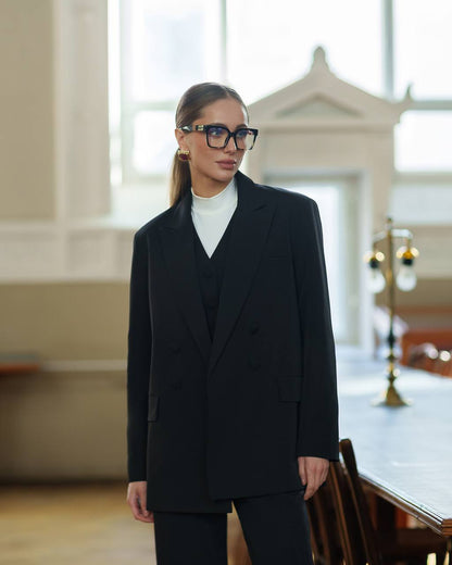 Woman wearing a black suit and glasses in an indoor setting