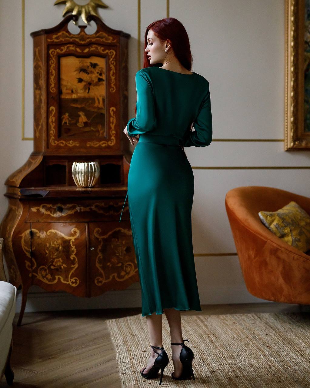 Woman in a green dress standing in an elegant room with ornate furniture.