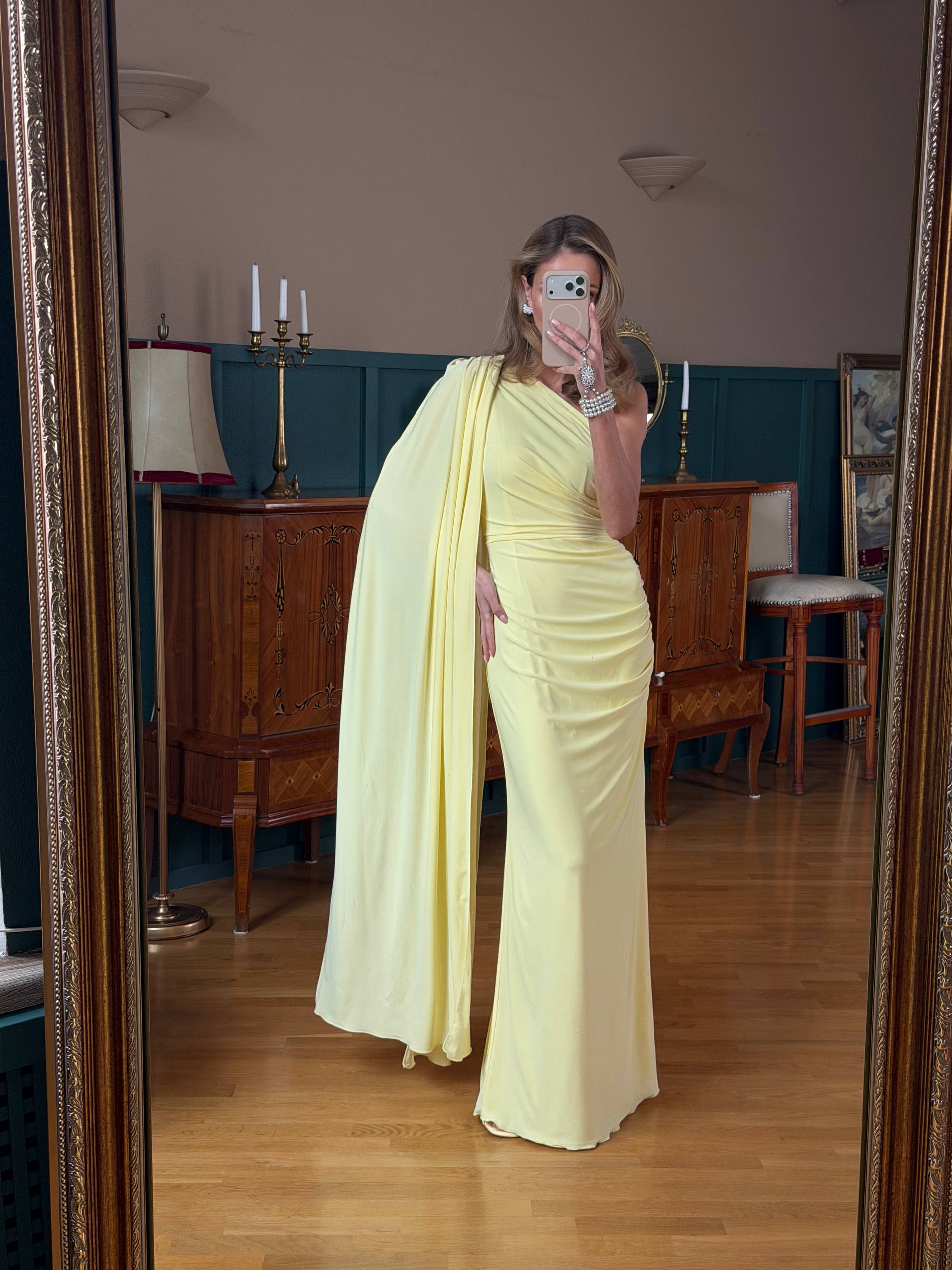 Woman in a yellow dress taking a mirror selfie in an indoor setting.