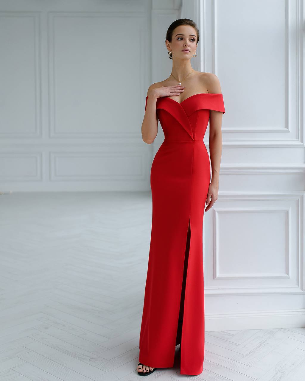 Woman wearing a red off-shoulder evening gown in a white room.