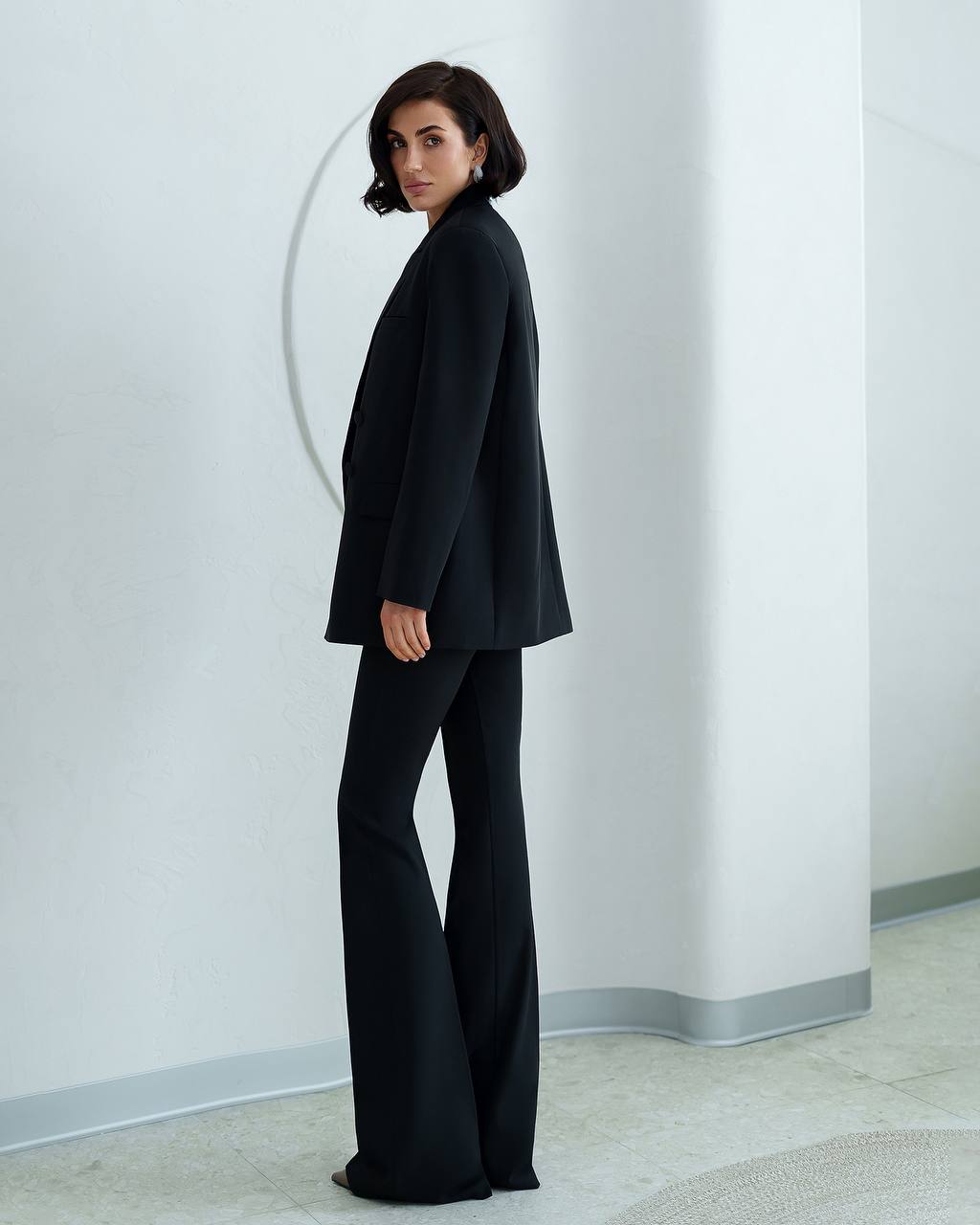 Woman wearing a black suit standing against a white wall