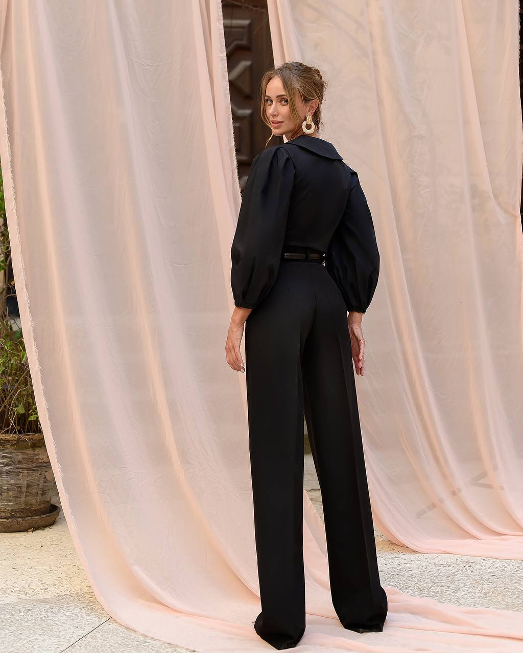 Woman in a black outfit standing in front of pink curtains