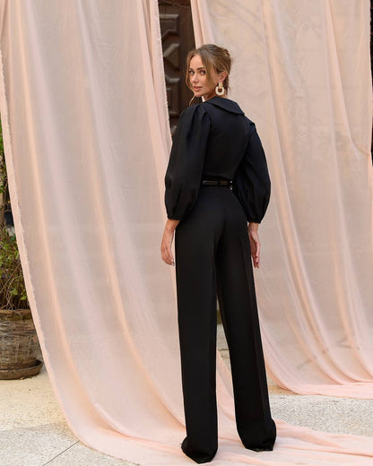 Woman in a black outfit standing in front of pink curtains