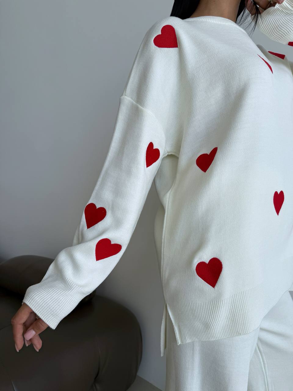 White sweater with red heart patterns worn by a person against a neutral background