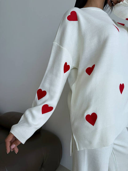 White sweater with red heart patterns worn by a person against a neutral background