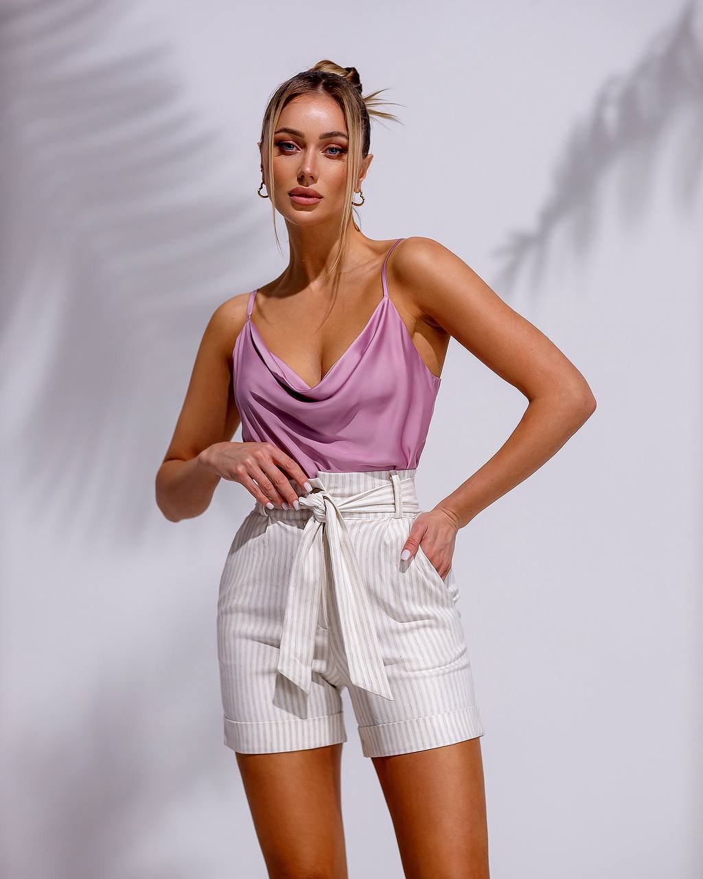 Woman wearing a pink top and white shorts against a plain background