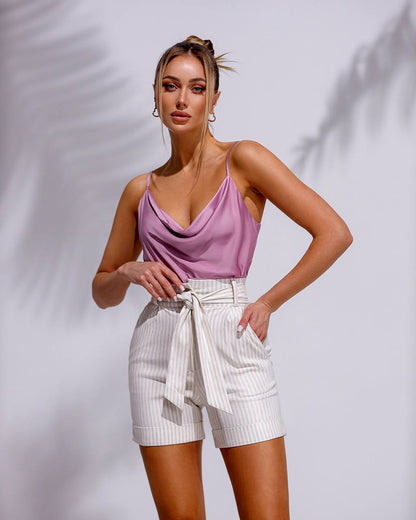 Woman wearing a pink top and white shorts against a plain background