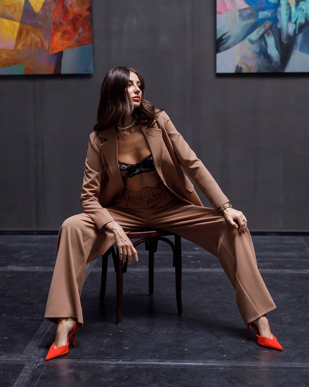 Woman in a beige suit sitting on a chair with abstract paintings in the background