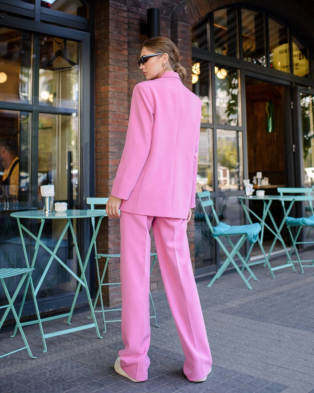 Person wearing a pink suit standing outside a building with green tables and chairs.