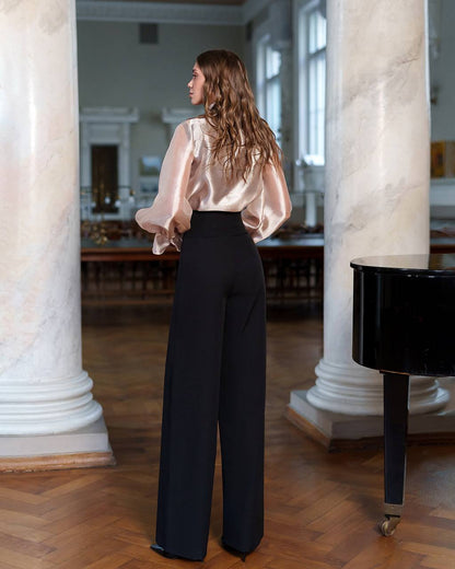 Woman in a beige blouse and black pants standing in a room with marble columns.