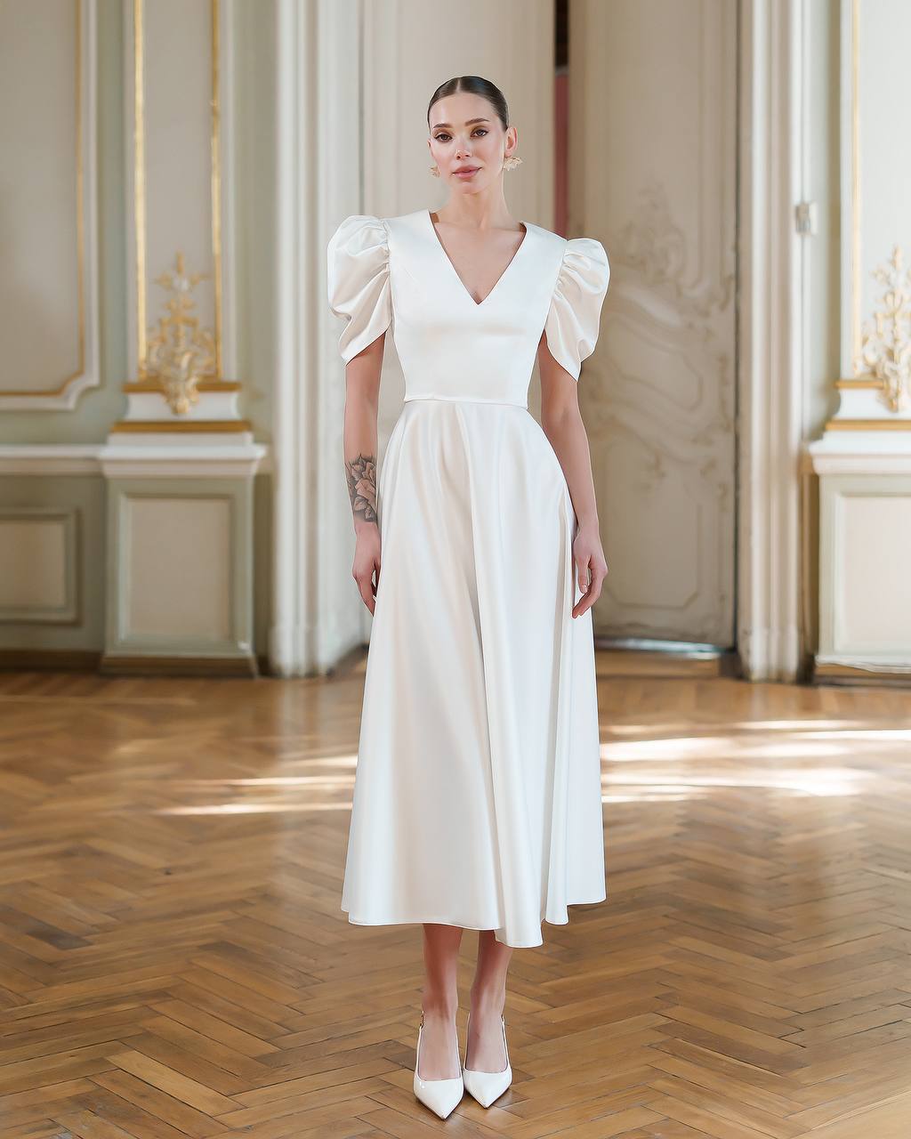 Woman wearing a white dress in an elegant room with wooden floor and decorative walls.
