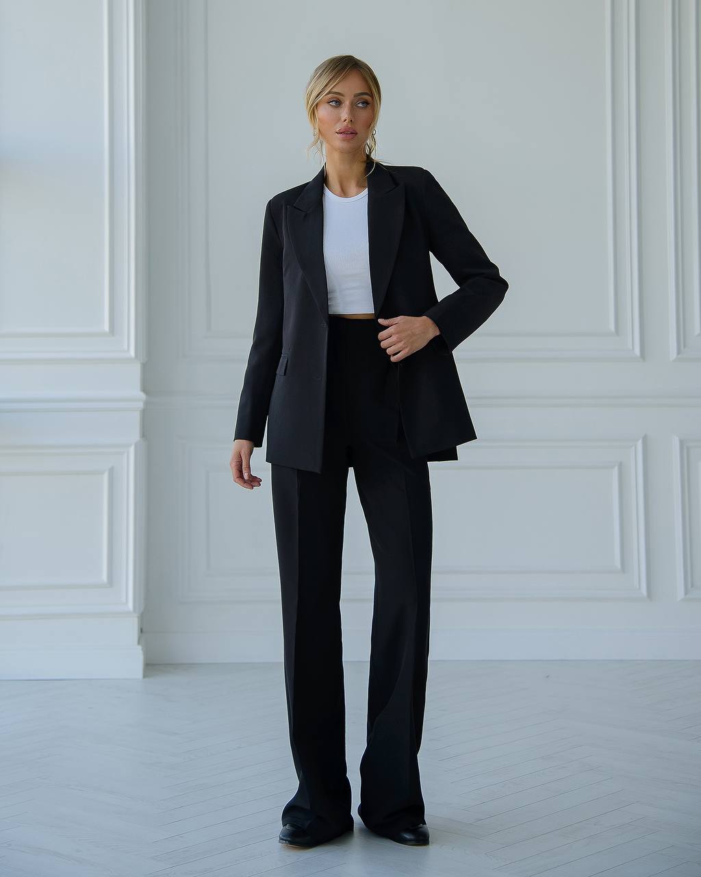 Person wearing a black suit and white shirt in a minimalistic room.