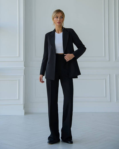 Person wearing a black suit and white shirt in a minimalistic room.