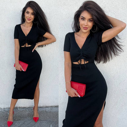 Woman wearing a black dress with cut-out design and red clutch against a white wall.