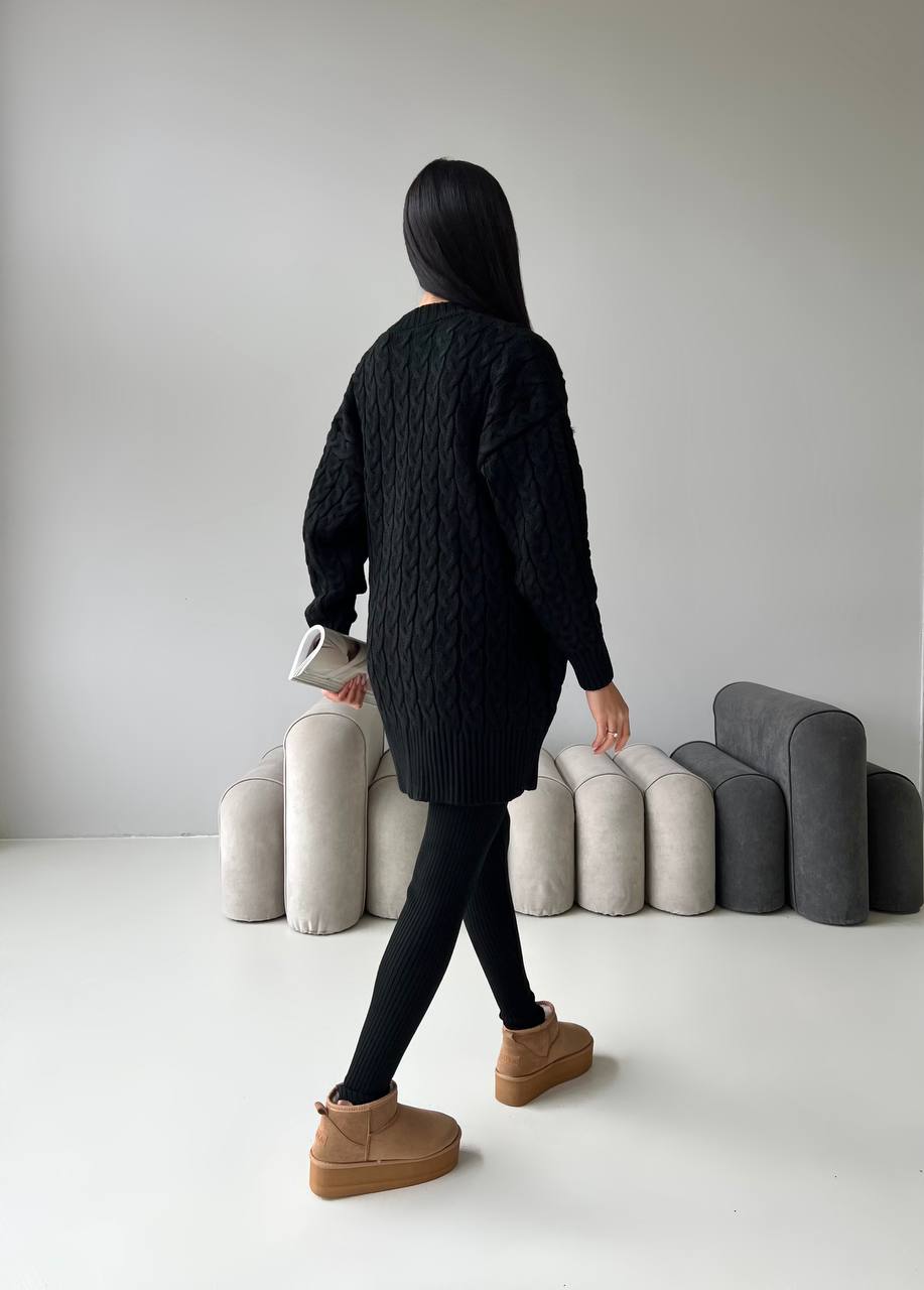 Person wearing a black quilted jacket standing in front of various textured cushions on a white floor.