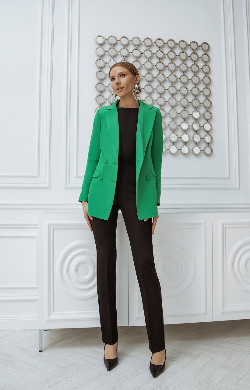 Woman wearing a green blazer over a black outfit in an elegant interior setting.