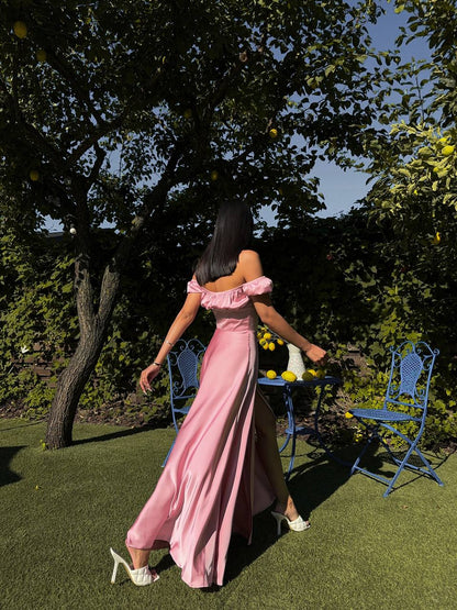 Woman in a pink dress walking in a garden with blue chairs and a table.