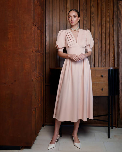 Woman in a pink dress standing in a room with wooden paneling.