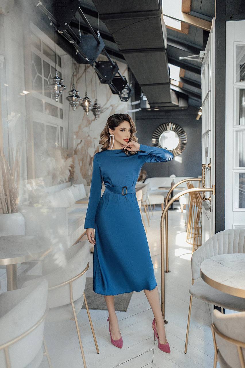 Woman in a blue dress posing in a modern cafe.