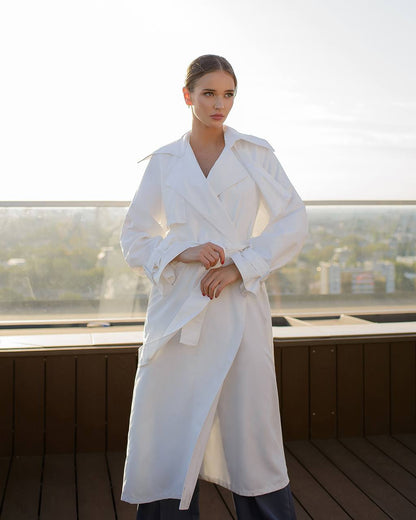 Woman wearing a white trench coat on a rooftop with a cityscape background