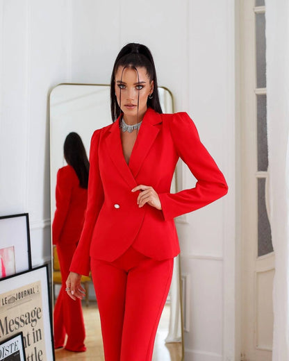 Woman wearing a red suit standing in a room with a mirror and framed picture.