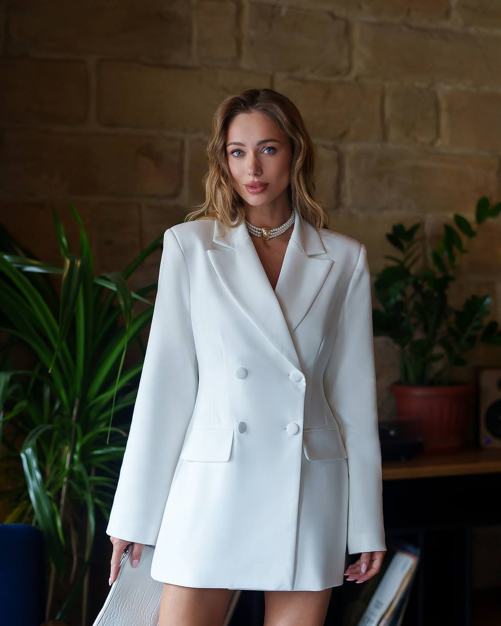 Woman wearing a white blazer and skirt set in an indoor setting with plants.